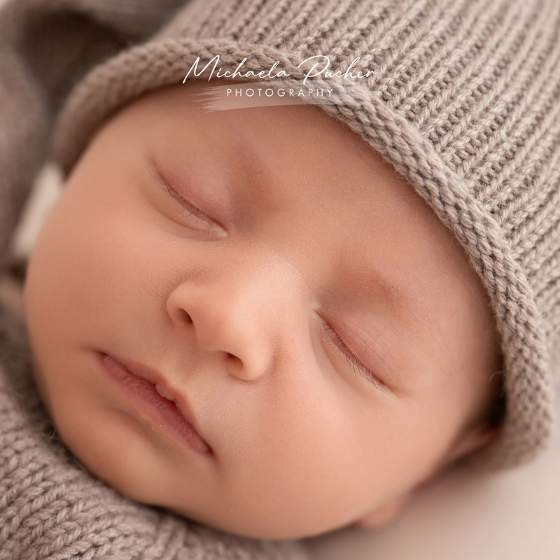 Nahaufnahme eines schlafenden Neugeborenen mit gestrickter Mütze in warmen Naturtönen.